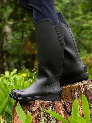 Closeup of a hiker's legs in black knee-high rubber boots standing on a tree stump